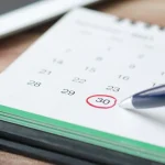 Рука з ручкою позначає дату на календарі, підкреслюючи планування та організацію.