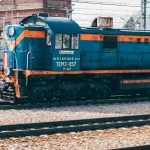 Яскравий синій локомотив на залізничних коліях з вінтажним промисловим фоном.