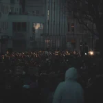 Великий натовп зібрався на протестному мітингу на слабо освітленій вулиці.