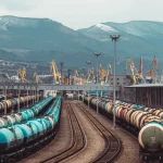 Довгі вантажні поїзди з контейнерами на залізничній станції з кранами та горами на фоні