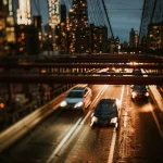 Нічний вид місту з підвісним мостом, автомобілями та яскравими вогнями на фоні міської панорами.