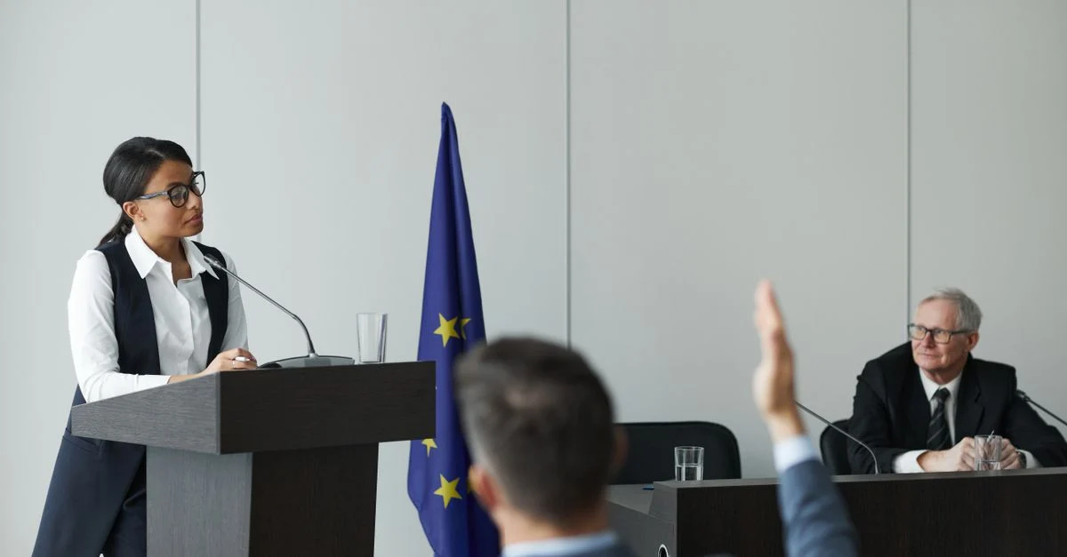 Жінка говорить на конференції ЄС, слухачі уважно її слухають.