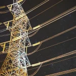 Освітлений енергетичний стовп на тлі зоряного нічного неба, демонструє інфраструктуру енергетики.