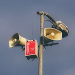 Пам'ятка з гучномовцями на стовпі проти хмарного неба, що попереджає про надзвичайні ситуації.