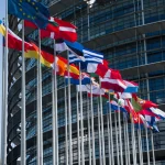 Державні прапори країн Європейського союзу перед сучасною фасадою будівлі.